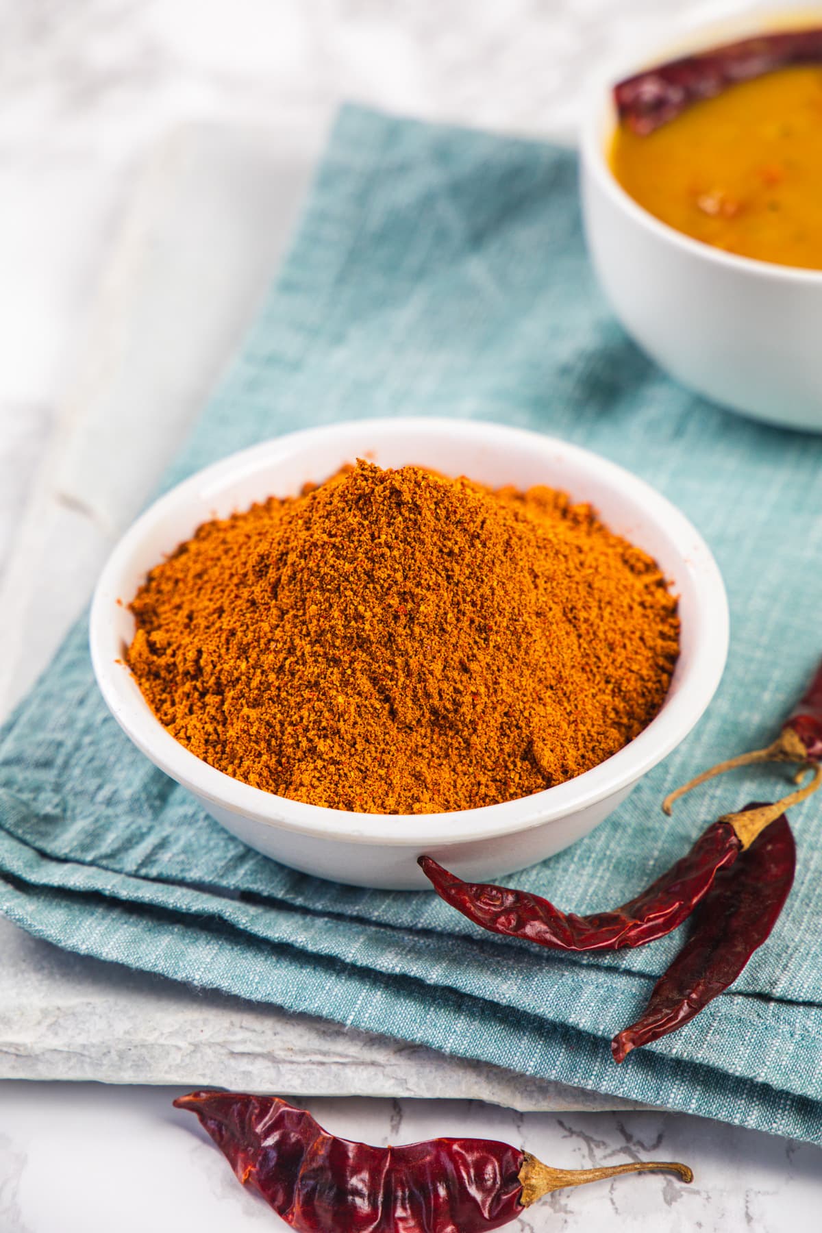 Sambar powder in a bowl with dried chilies and sambar bowl on the side and napkin under it.