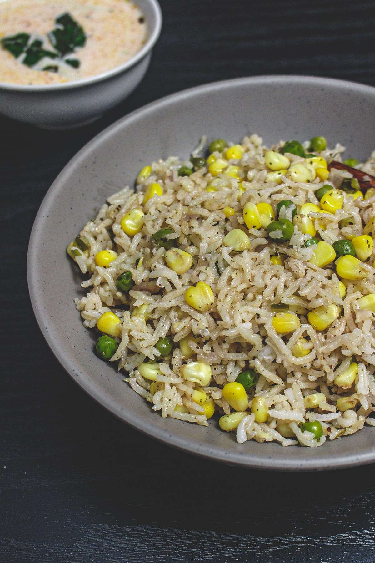 A bowl of corn pulao with a bowl of raita.