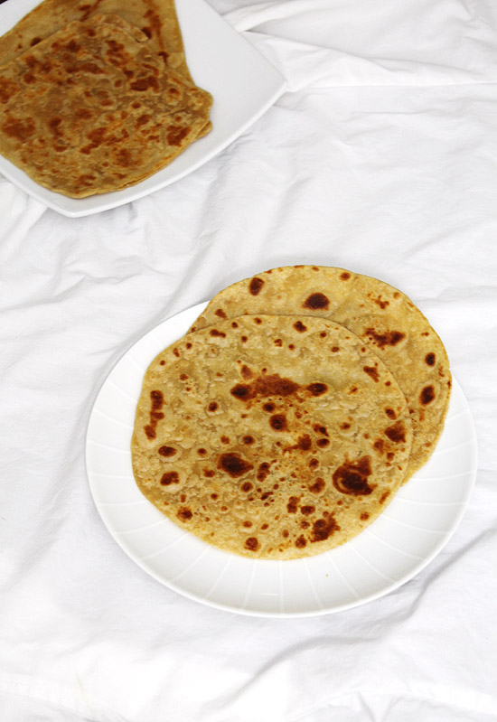 Plain paratha served in a plate with few more paratha in the back.