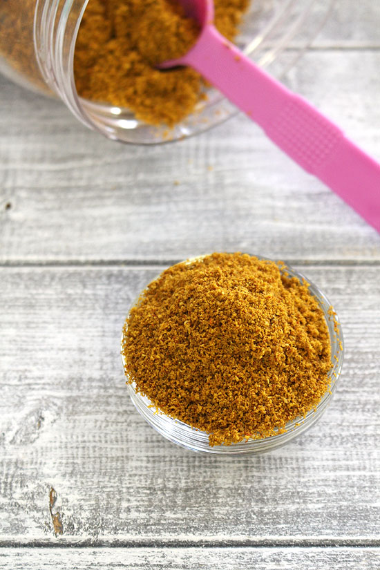Sambar powder in a bowl with container with spoon in the back.
