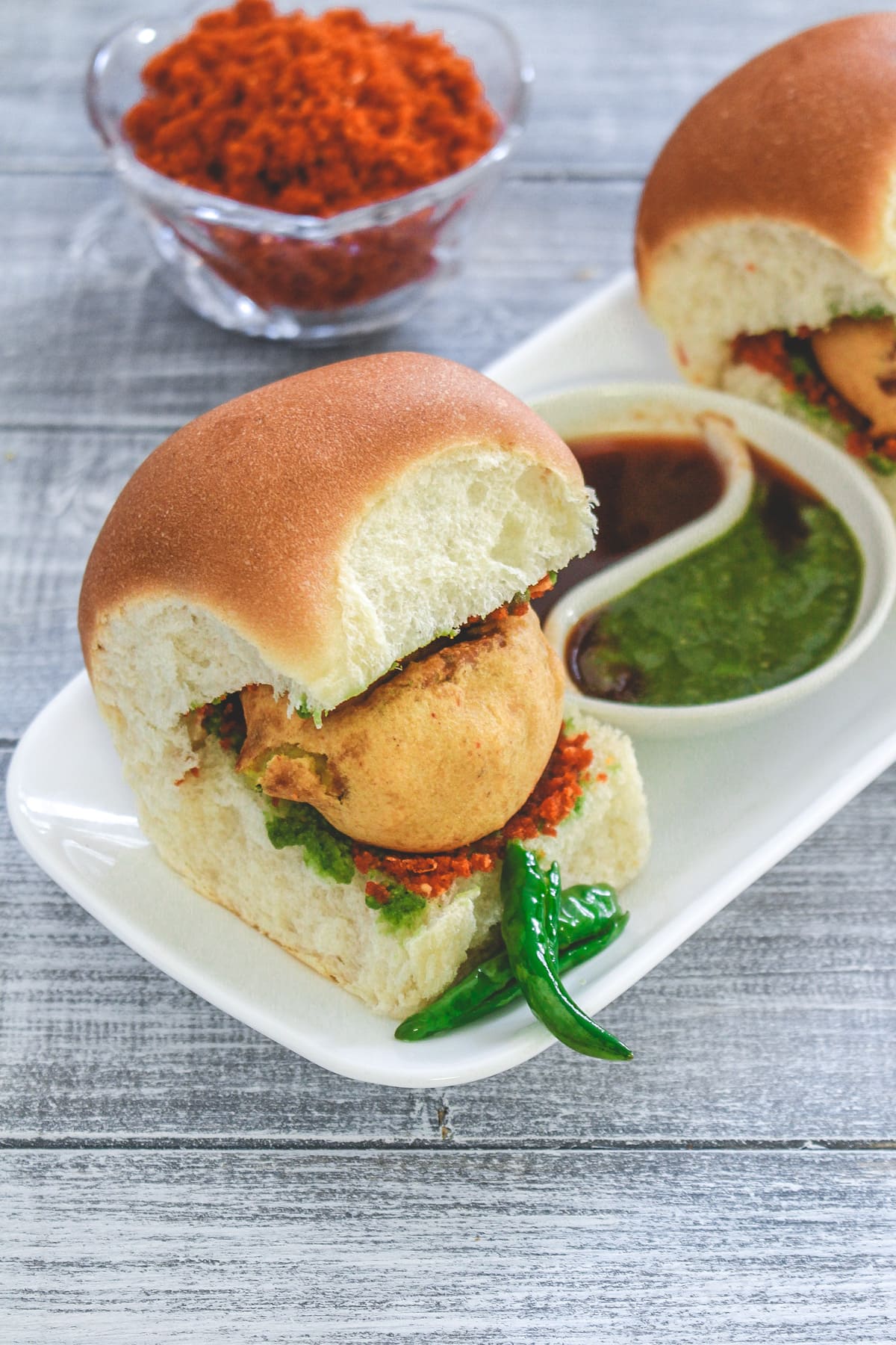 Vada pav served with fried green chili and 3 chutneys.