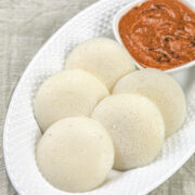 5 idli served with chutney in an oval plate.