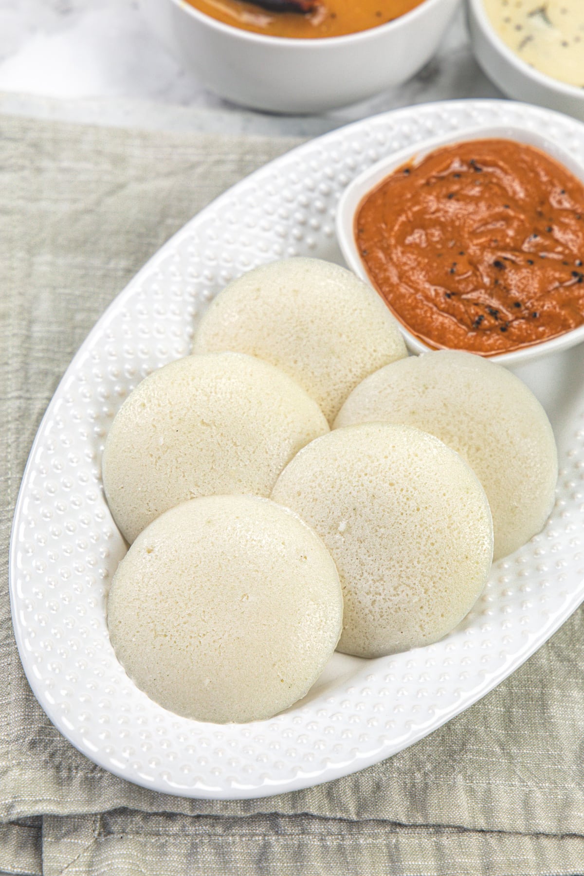 5 idli served with chutney in an oval plate.