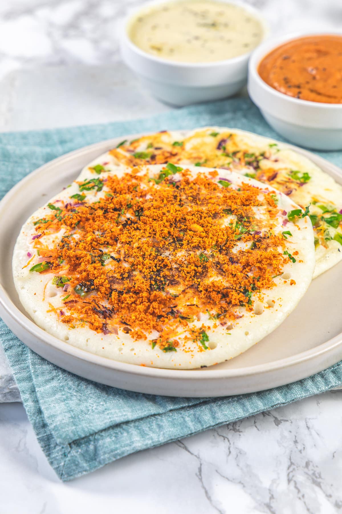 Uttapam topped with idli podi served with chutneys.