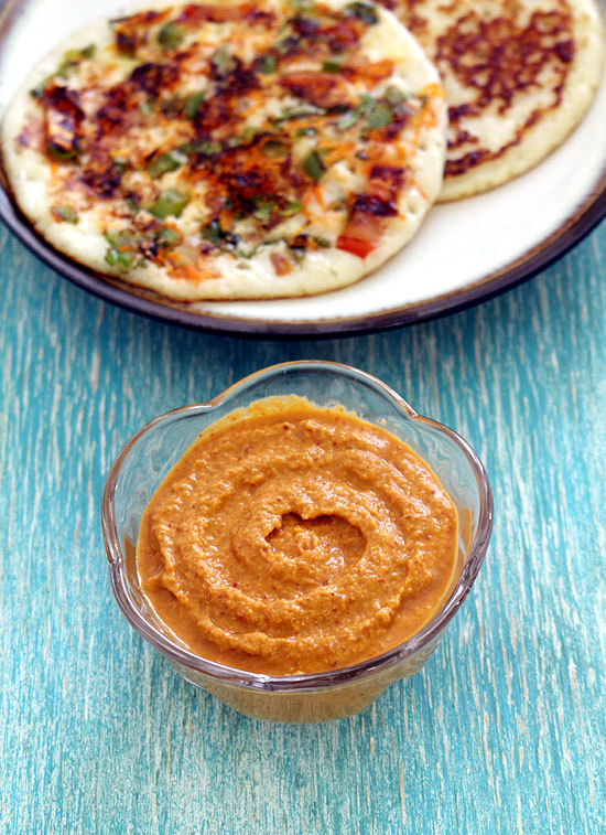 Red coconut chutney in a bowl with uttapam in the back.