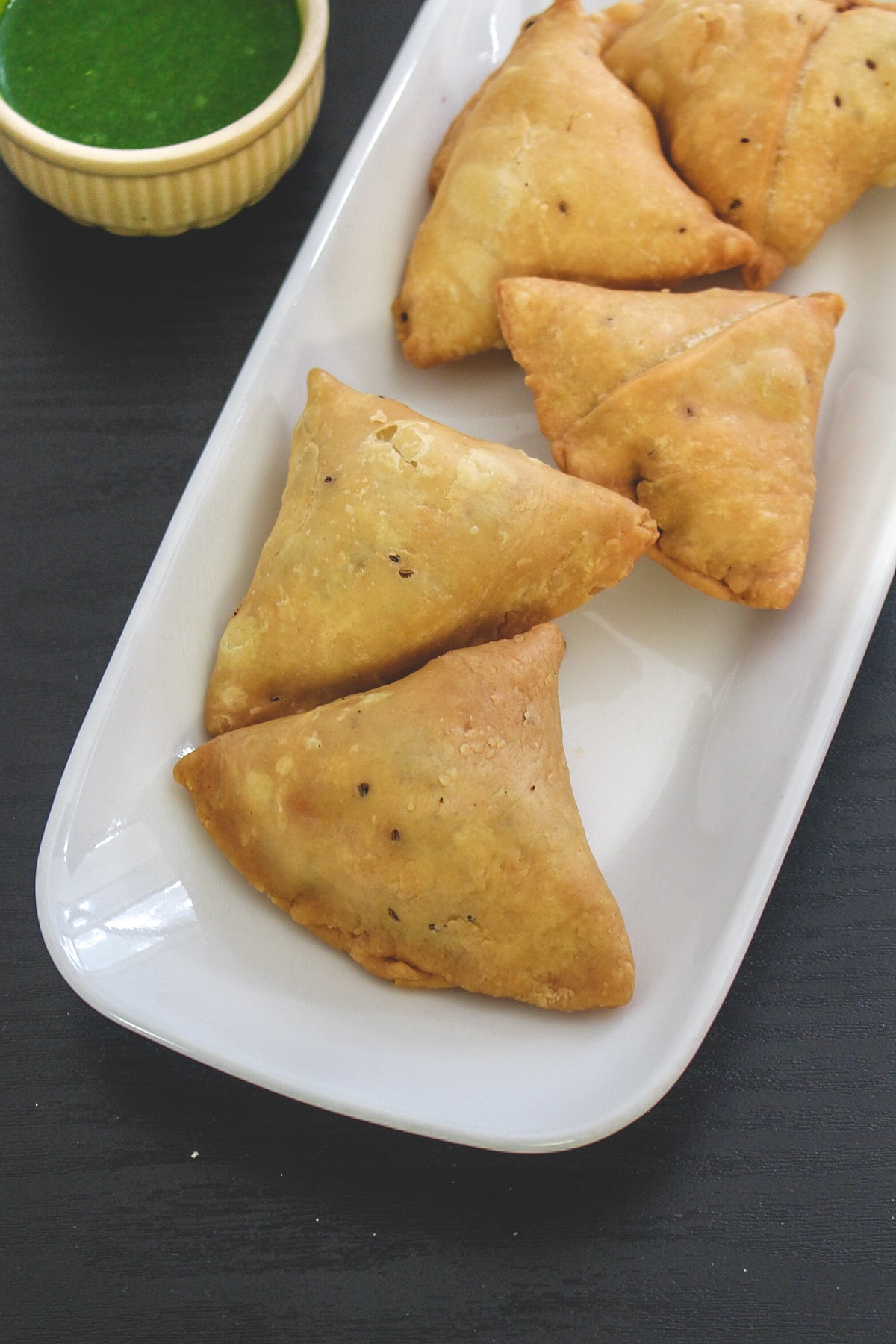 5 aloo samosa in a plate with a small bowl of green chutney.