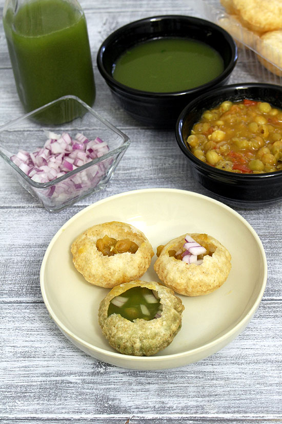 3 ragda pani puri in a plate with ragda bowl, onion and extra pani in the back.