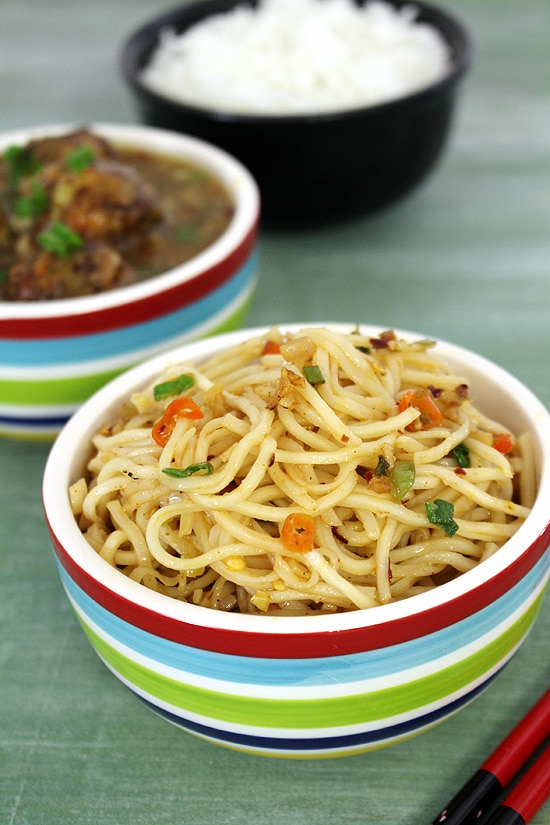 Chilli garlic noodles in a bowl with manchurian gravy dish and rice in the back.