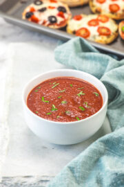 Pizza sauce in a bowl garnished with chopped basil leaves.