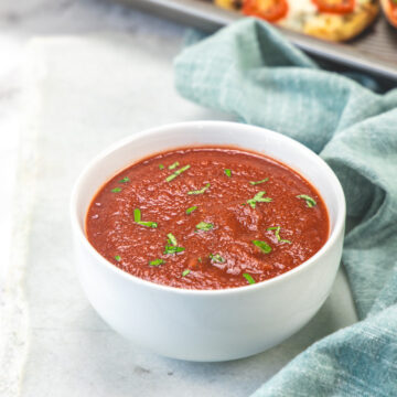 Pizza sauce in a bowl garnished with chopped basil leaves.