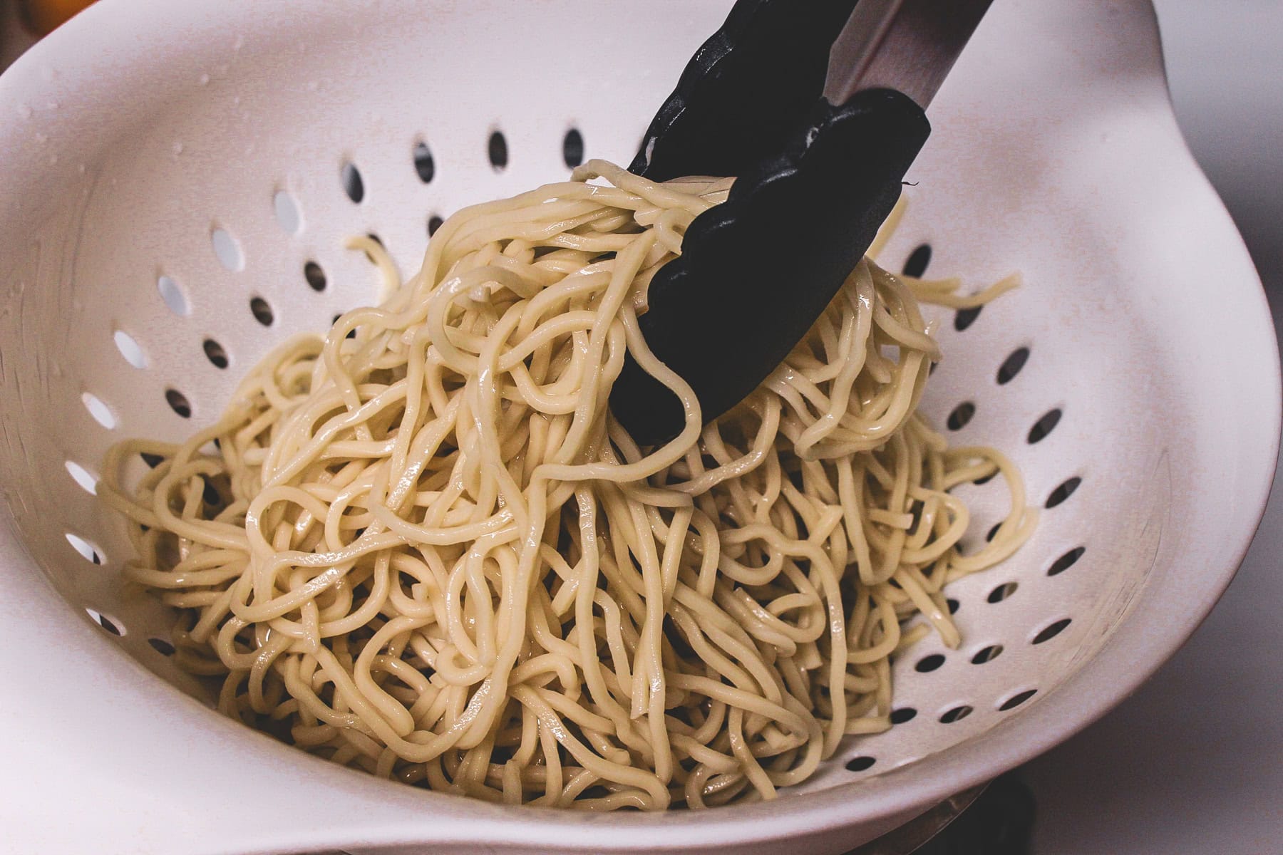 Tossing noodles to coat oil evenly.