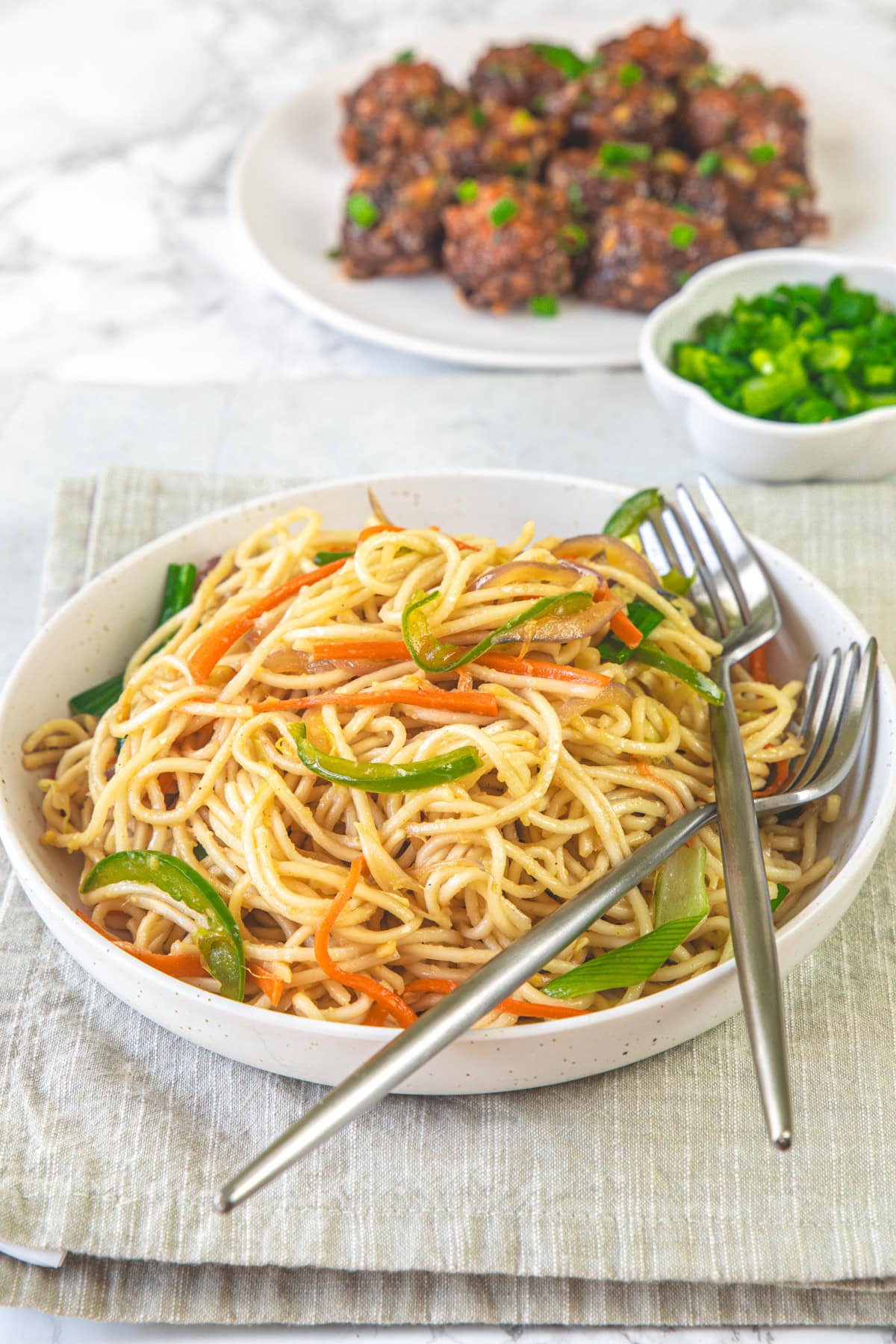 Veg hakka noodles in a bowl with forks and manchurian served in the back.