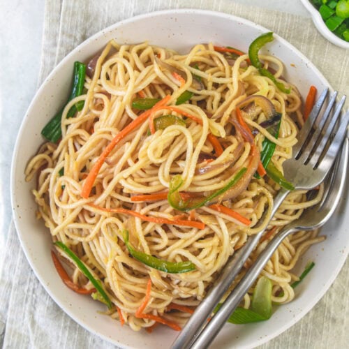 A bowl of veg hakka noodles with two forks on a napkin.