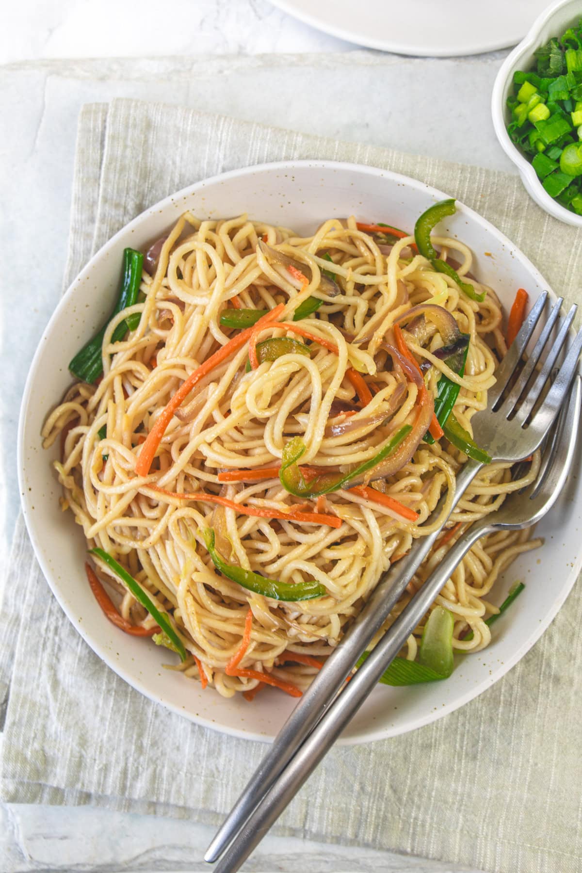 A bowl of veg hakka noodles with two forks on a napkin.