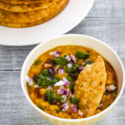 Dal in a bowl with chutneys and onion, scooping with pakwan.