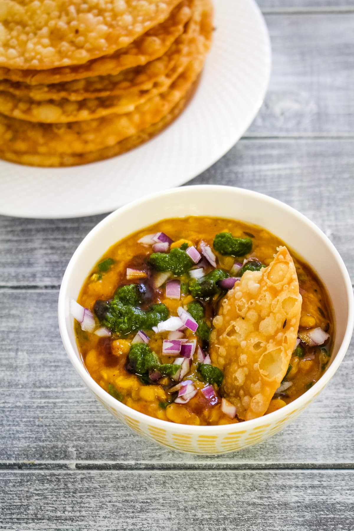 Dal in a bowl with chutneys and onion, scooping with pakwan.