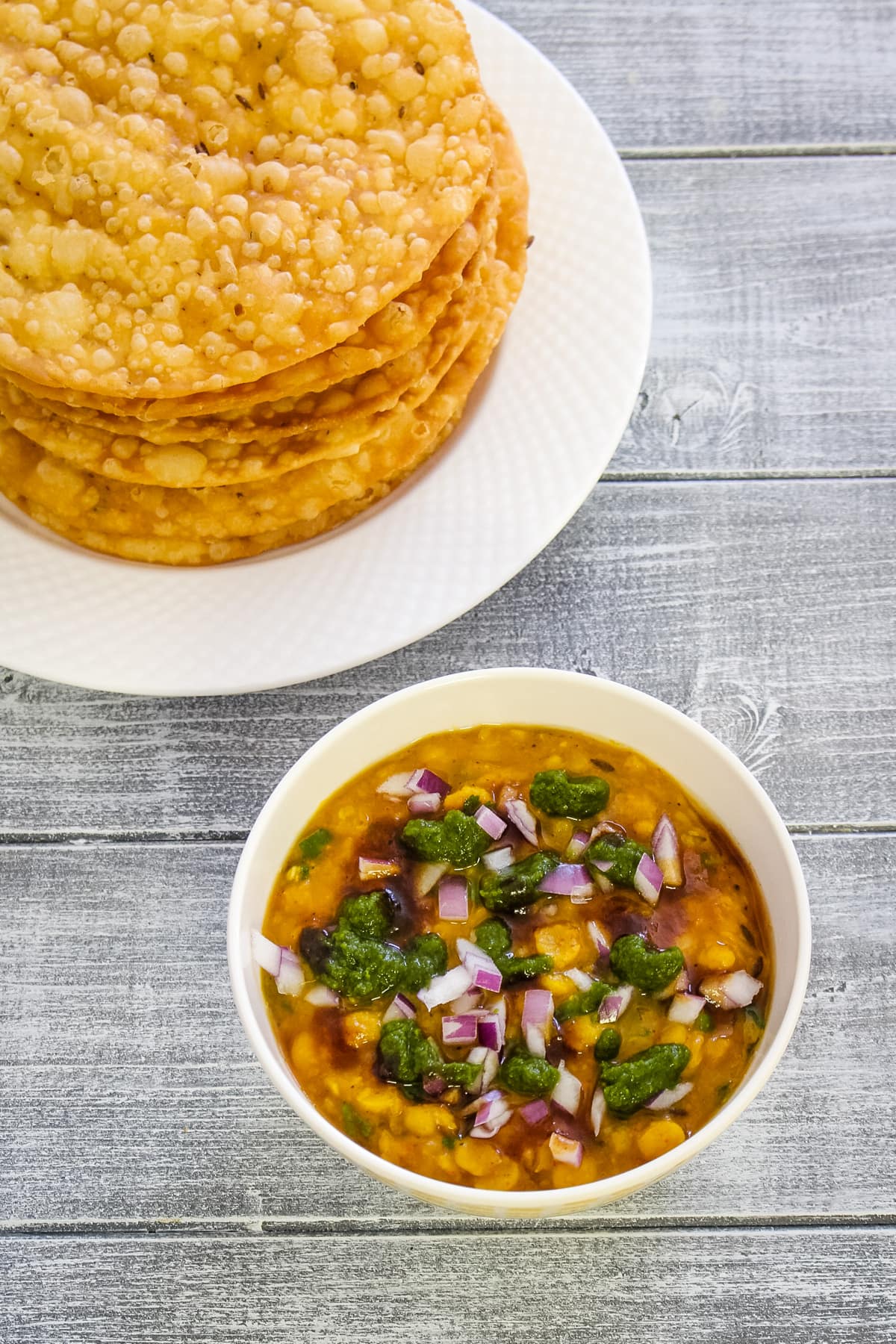 Dal pakwan is served with a bowl of dal with toppings of chutney and onion.