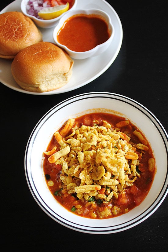 Misal garnished with farsaan and pav, kat and onion in the back.