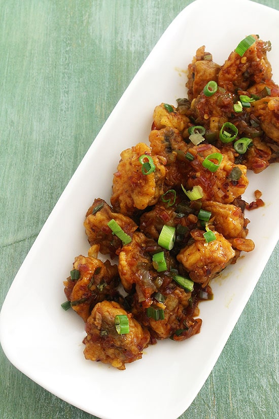 Mushroom manchurian served in a plate with a garnish of spring onion greens.