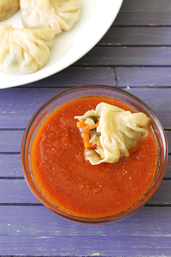 A half veg momo in a bowl of sauce.