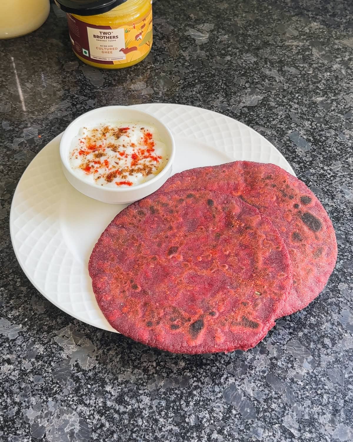2 beetroot paratha served with a bowl of yogurt.