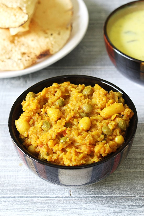 Vaghareli khichdi served in a bowl with a bowl kadhi and roasted papad in the back.