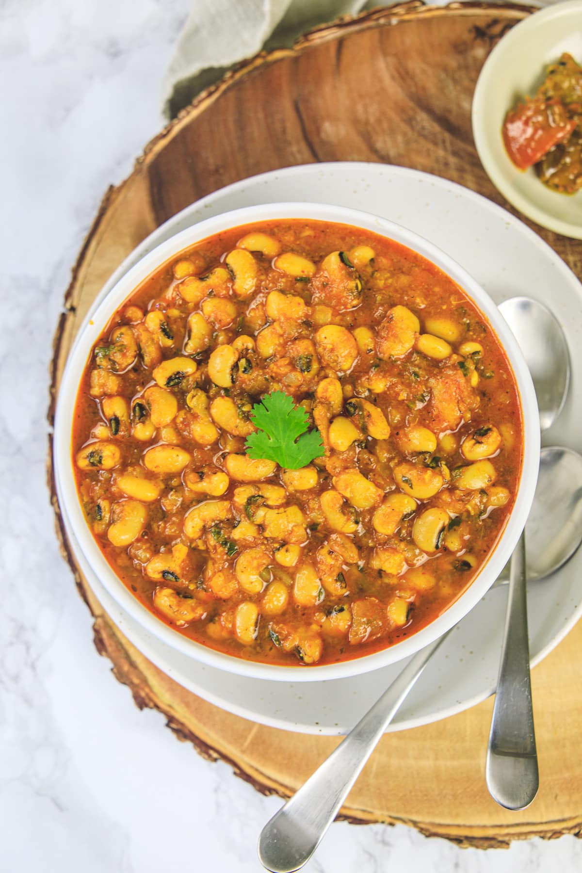 Black eyed peas curry in a bowl garnished with cilantro and 2 spoons on the side.