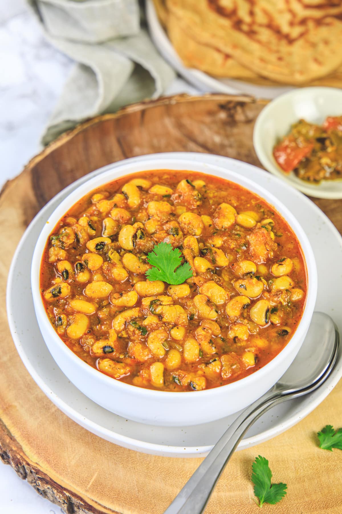 Lobia masala in a bowl with spoons, pickle and paratha on the side.