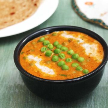 Matar masala garnished with cooked peas and cream, served with paratha in the back.