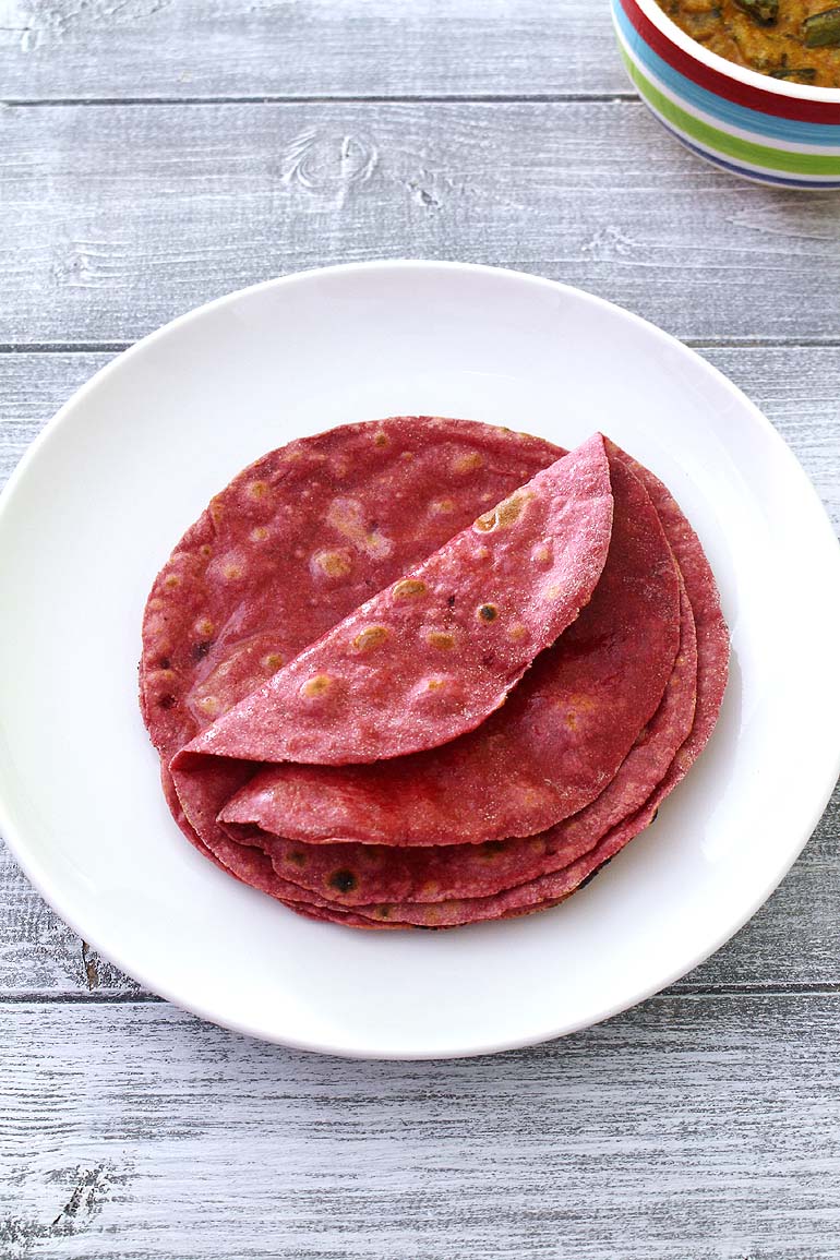 Beetroot roti served in a plate with a bowl of sabji in the back.