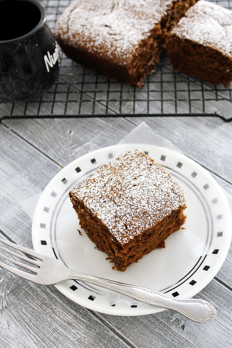 Eggless gingerbread cake slice in a plate dusted with powdered sugar.