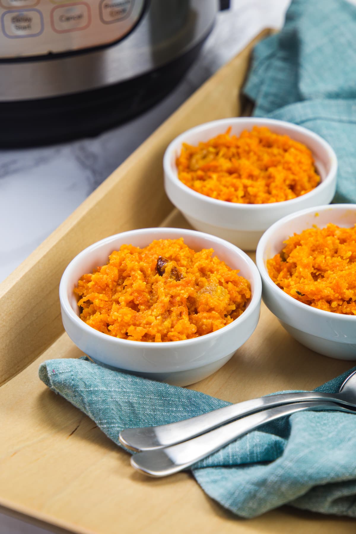 3 bowls of carrot halwa in a tray with spoons and instant pot in back.