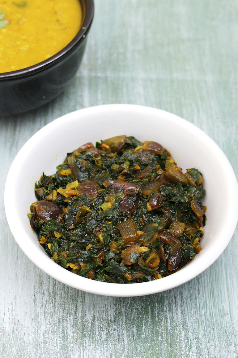 Methi sabzi served in a white bowl with a bowl of dal in the back.