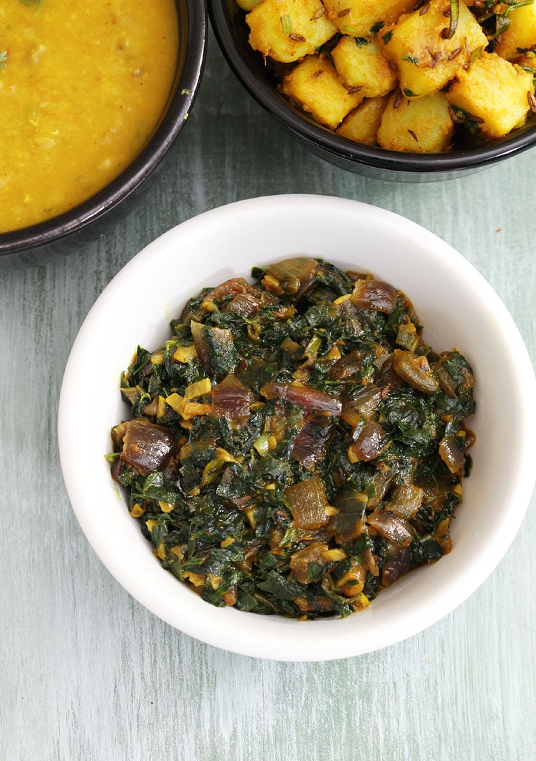 Methi bhaji served in a bowl with jeera aloo and dal served in the back.