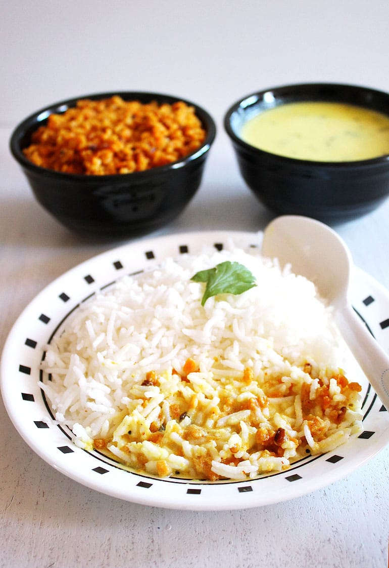 Sookhi moong dal mixed with kadhi and rice in a plate with a spoon and exta moong dal and kadhi bowl in the back.