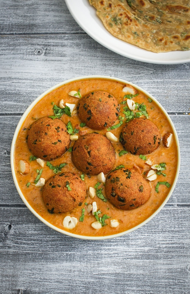 Paneer kofta curry served in a plate and garnished with cashews and cilantro.