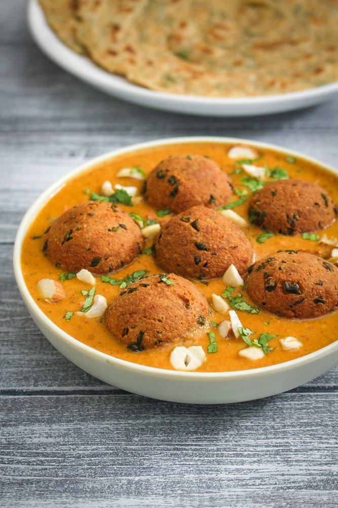 Paneer kofta curry garnished with cilantro and chopped cashews.