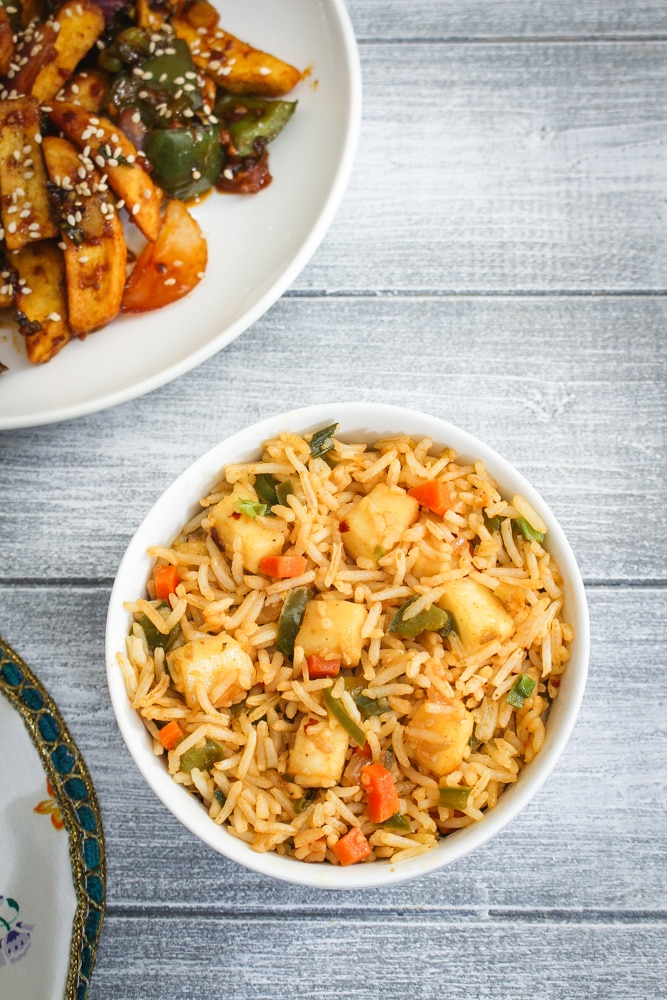 Paneer Fried Rice served in a bowl with honey chili potatoes in the back.