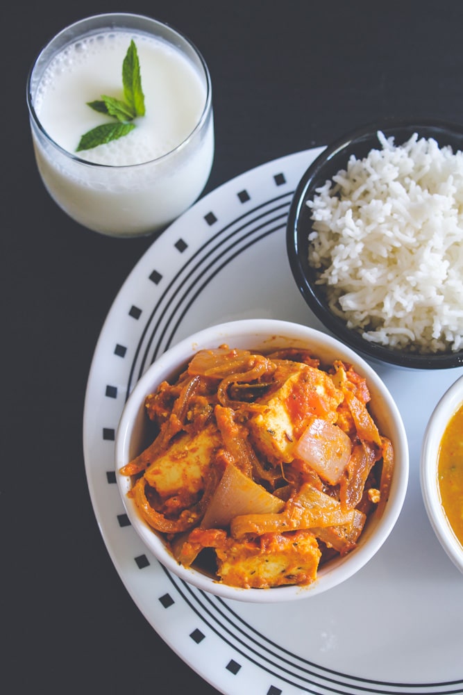 Paneer do pyaza in a bowl with a side of rice and a glass of chaas.