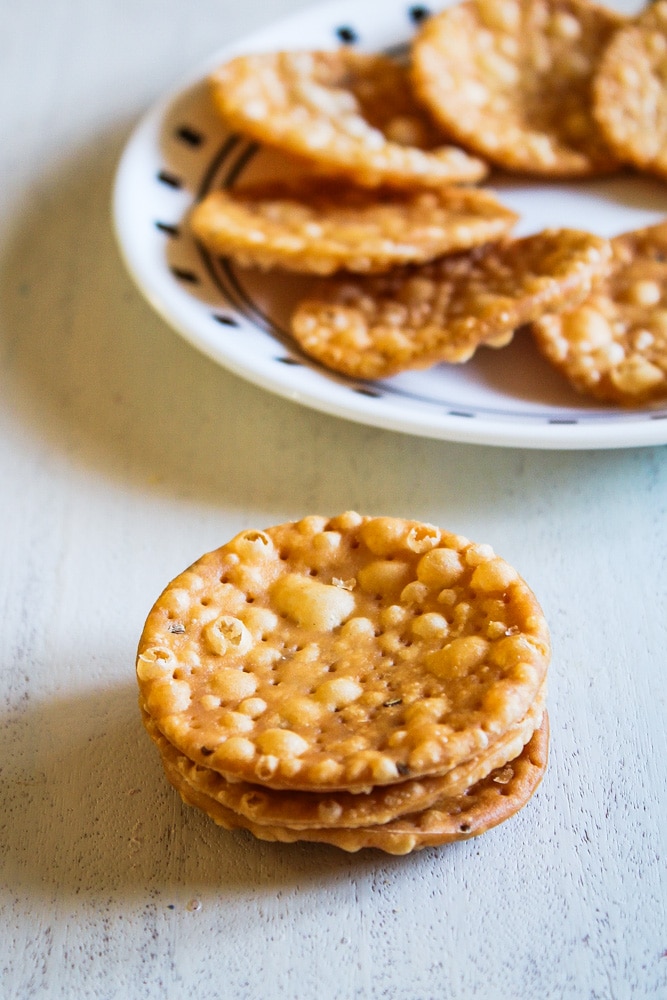 Stack of papdi on a wooden board with a plate of papdi in the back.