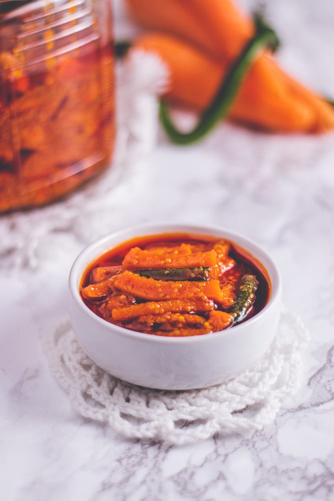 Carrot pickle in a small bowl with jar in the background.