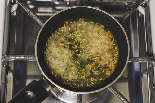 adding cumin seeds to the tadka