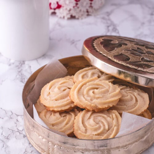 Eggless butter cookies in a container with coffee in the back.