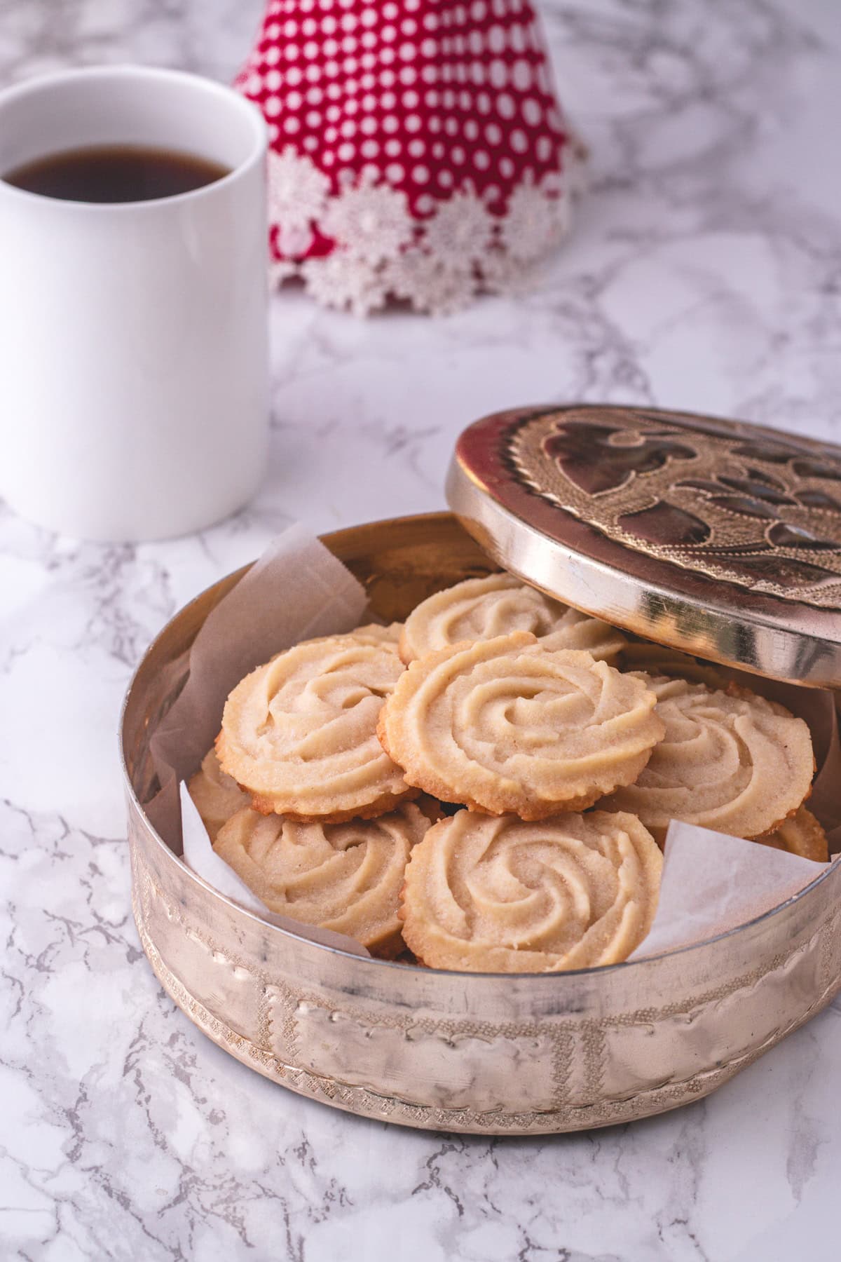 Eggless butter cookies in a container with coffee in the back.