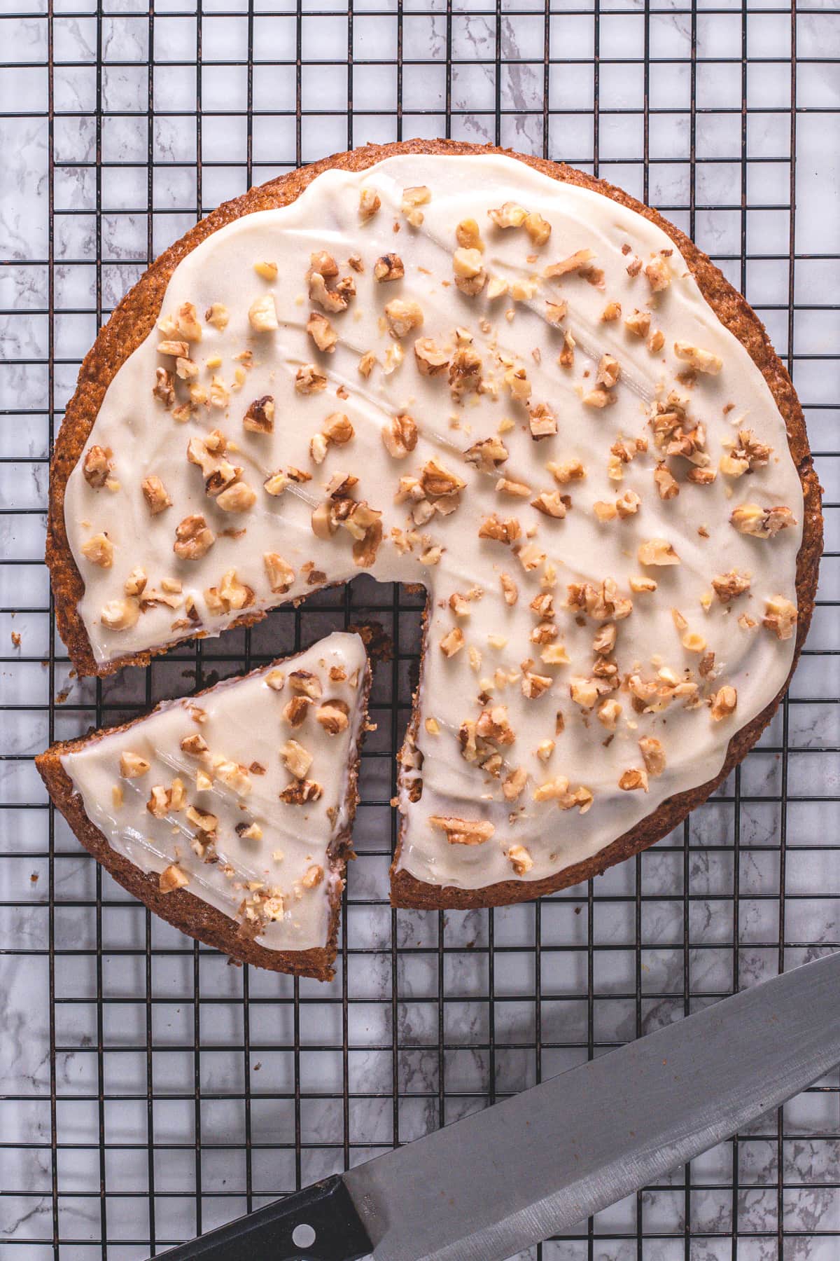 Eggless carrot cake with one slice on a cooling rack with a knife.