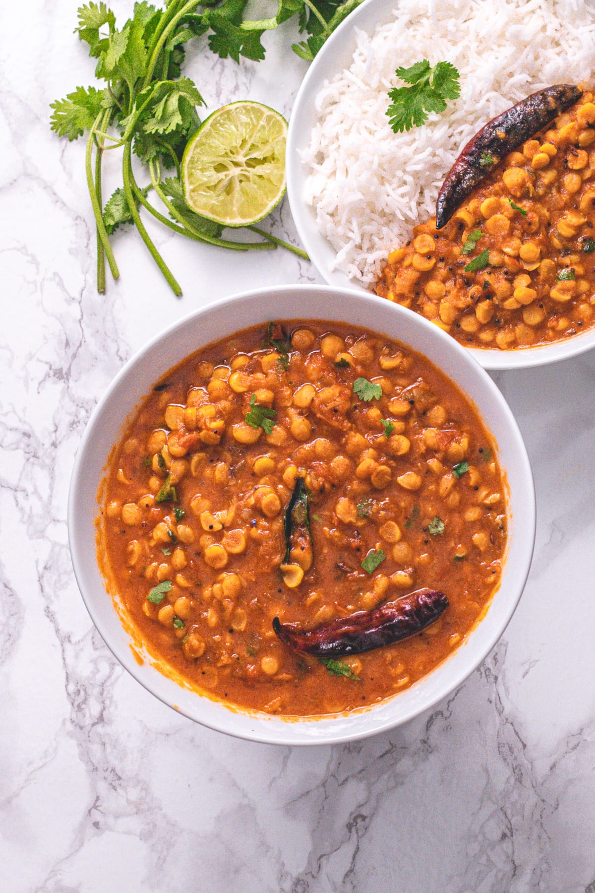 Chana dal bowl with another bowl of dal, rice with cilantro and lime slice on the side.