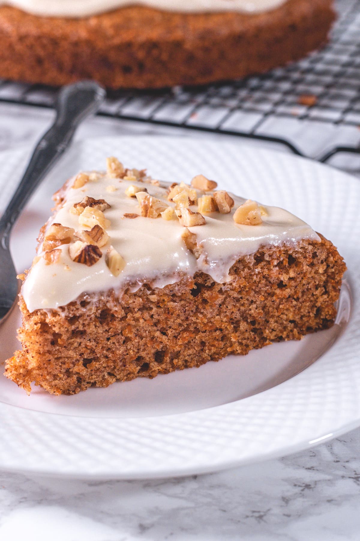 A slice of eggless carrot cake in a plate with fork.