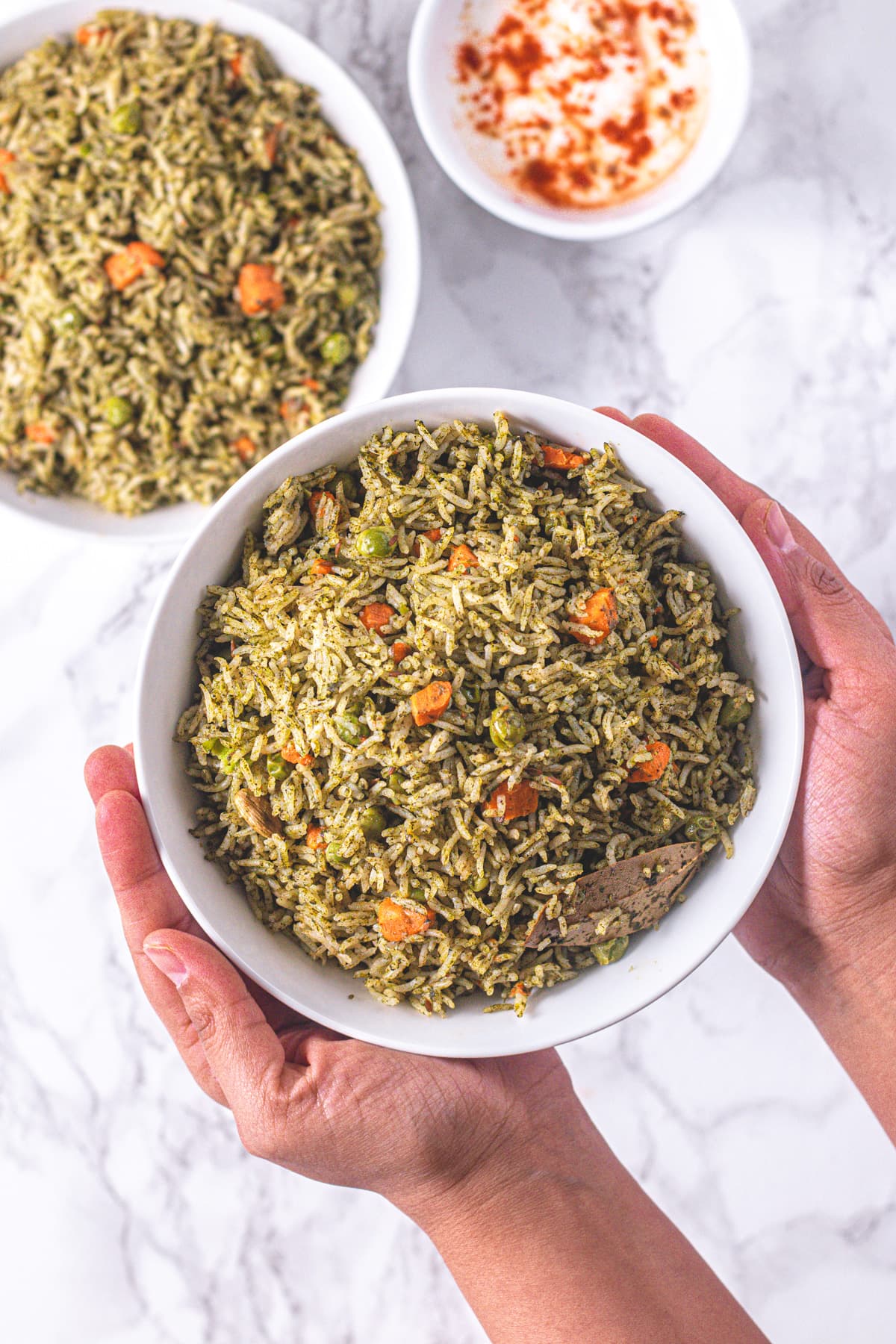 A bowl of palak rice holding with two hands and another bowl in the back.