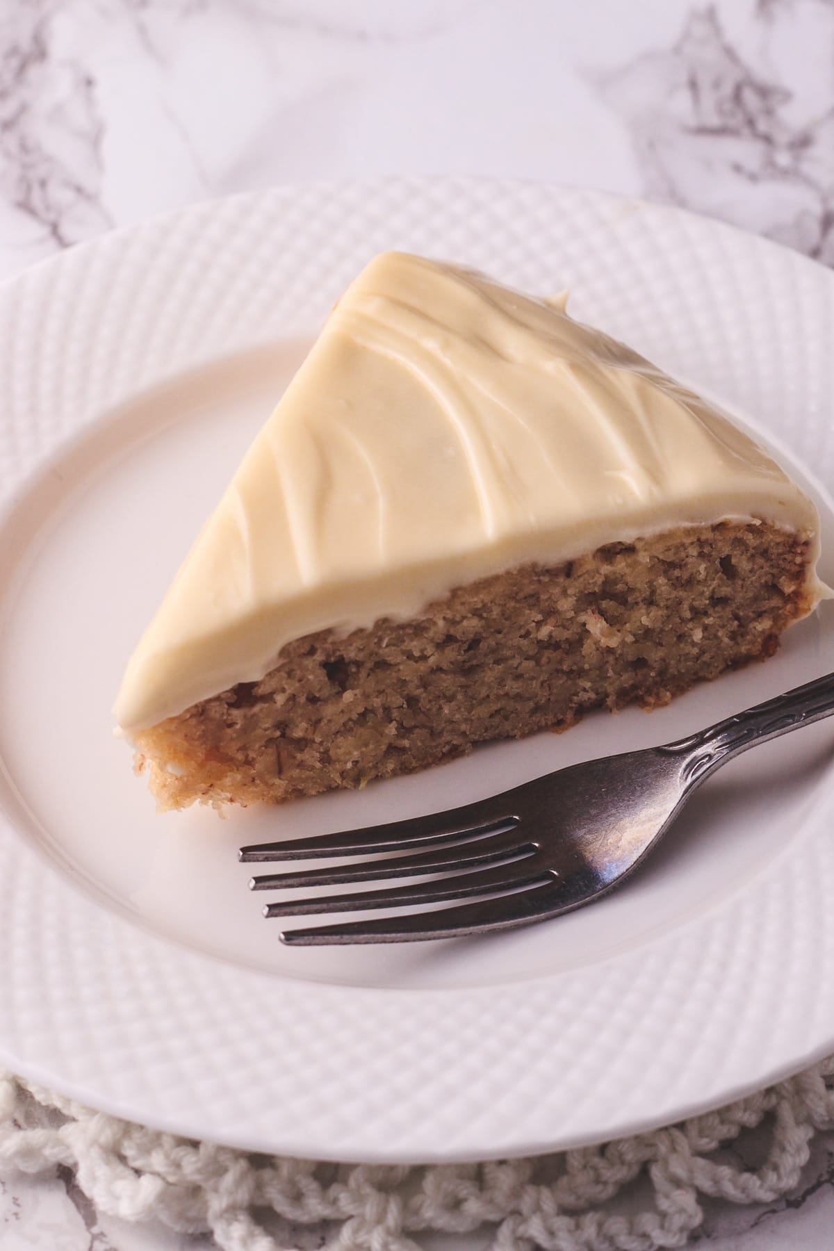 A slice of eggless banana cake in a white plate with fork.