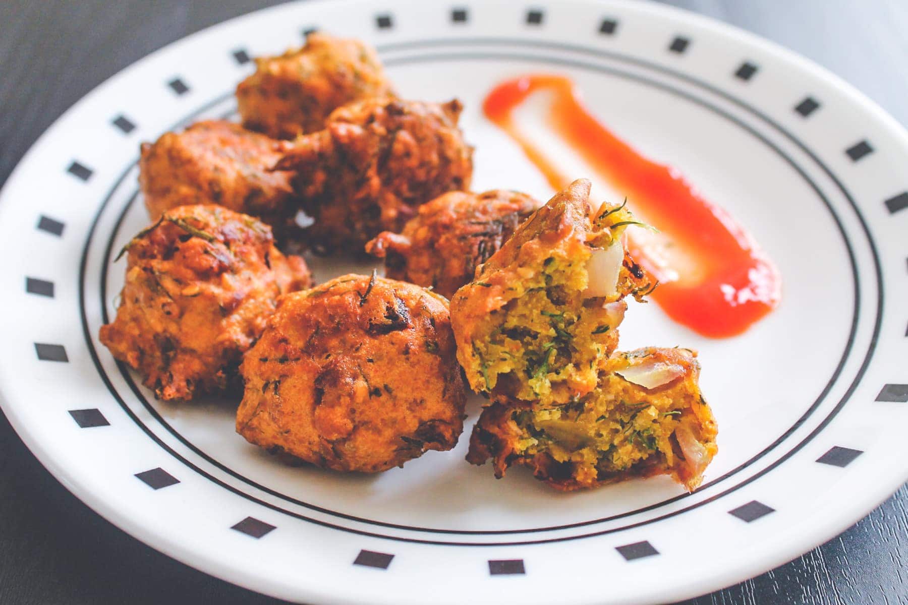 Dill leaves pakoda on a plate with one pakoda is shown inside part
